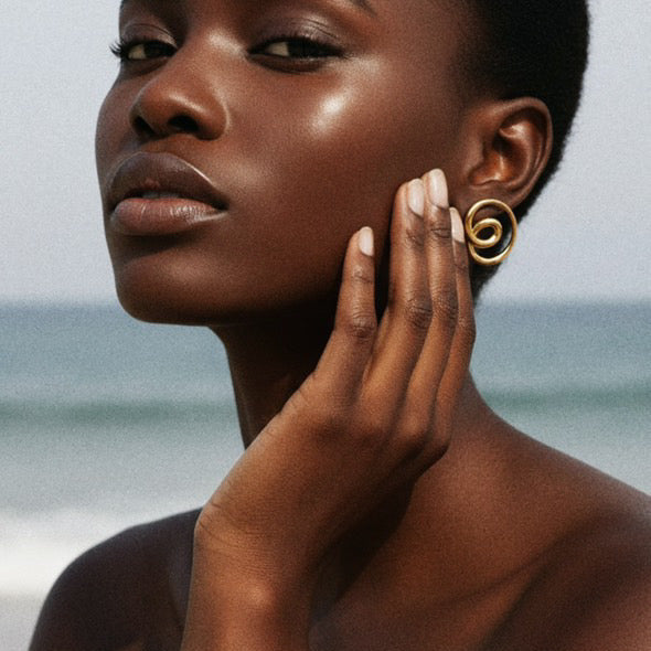 Woman wearing gold earrings and bracelet with a blurred ocean background